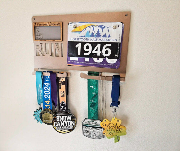 Personalized Running Achievement display with PR results, hanging Race Medals, and attached Race Bibs from 5Ks, 10s, Half-Marathons, and Marathons. Made from sturdy steel. Rose-Gold finish shown. 