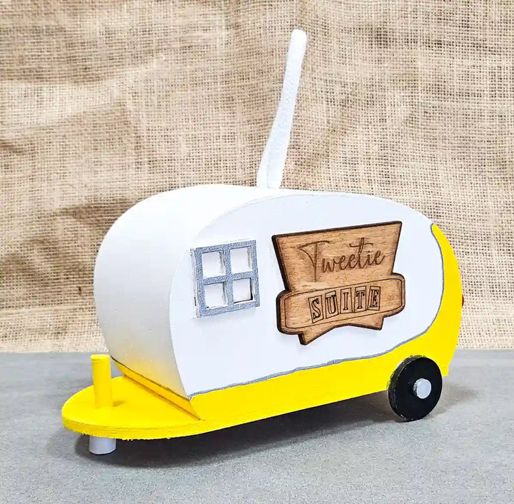 Retro camper birdhouse painted in a bright yellow color, featuring a sign reading 'Tweetie Suite' and detailed hand-painted accents.