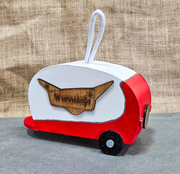 A bright red retro camper birdhouse with a sign reading 'Wrennabago' and a detailed spare tire cover, displayed against a light background.