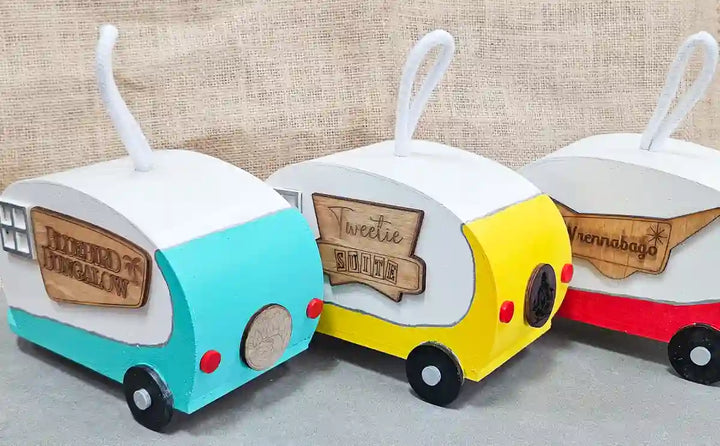 A group photo of all three retro camper birdhouses side by side, showcasing the different color variations and funny engraved name plates.