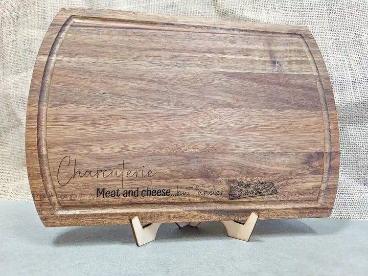 Rectangular Acacia wood charcuterie board with rounded corners, showing the engraved phrase 'Charcuterie. Meat and cheese...but fancier' against a light background.