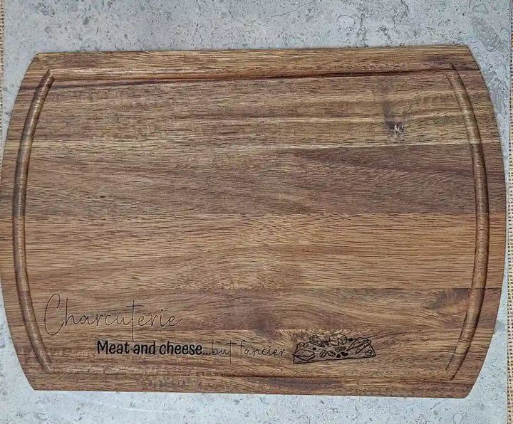 Close-up of the natural wood grain and the engraved phrase on the rectangular Acacia wood charcuterie board.