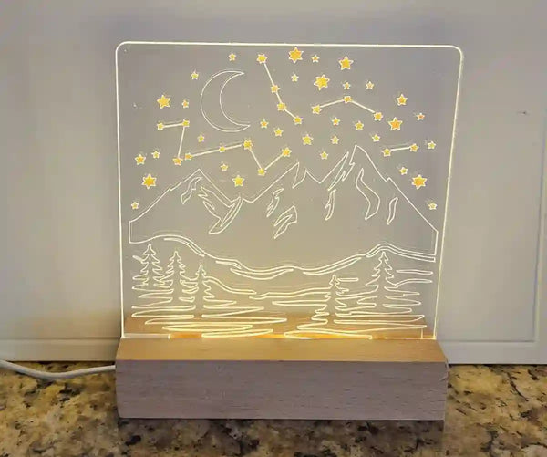 Clear acrylic nightlight with engraved mountain range, crescent moon, stars, and a constellation, illuminated by a light base.