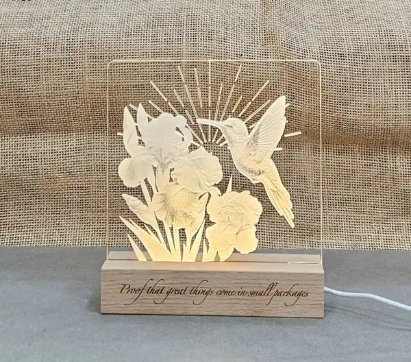 Clear acrylic nightlight with engraved hummingbird and iris design, illuminated by a light base, with the engraved phrase 'Proof that great things come in small packages' visible on the base.